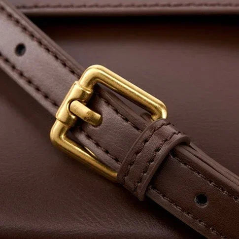 Brown leather strap with gold buckle on brown leather surface