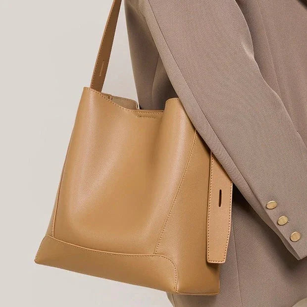 Tan leather bucket bag worn over a beige blazer, minimalist fashion accessory