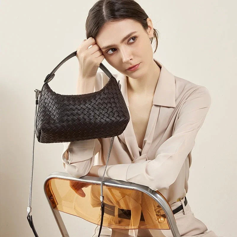 Woman in beige blouse holding black woven leather shoulder bag, sitting on chair
