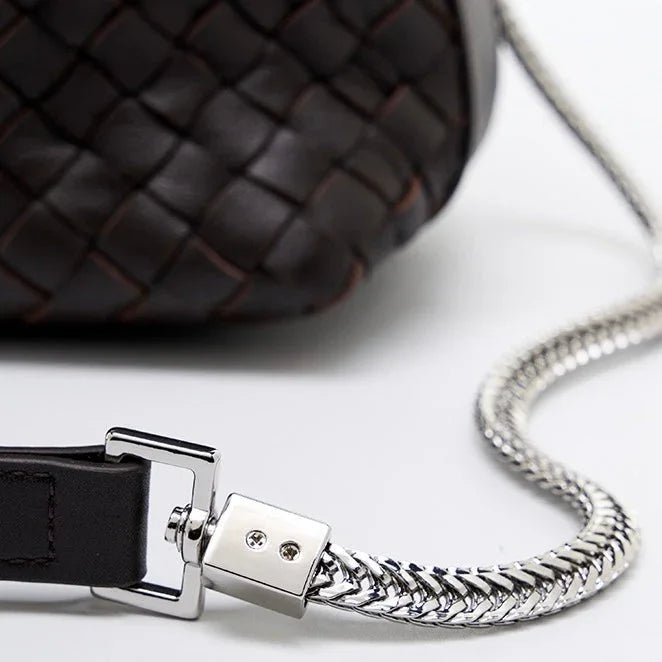 Close-up of woven dark leather bag with silver chain strap on white background
