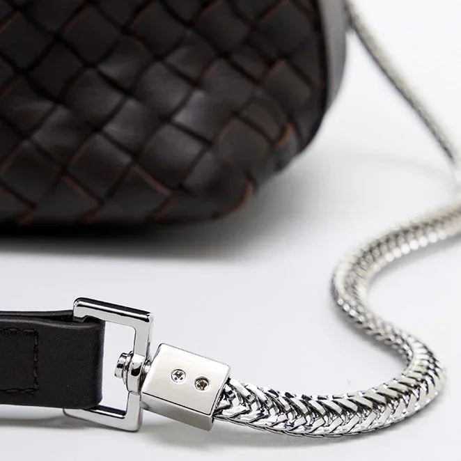 Close-up of woven dark leather bag with silver chain strap on white background