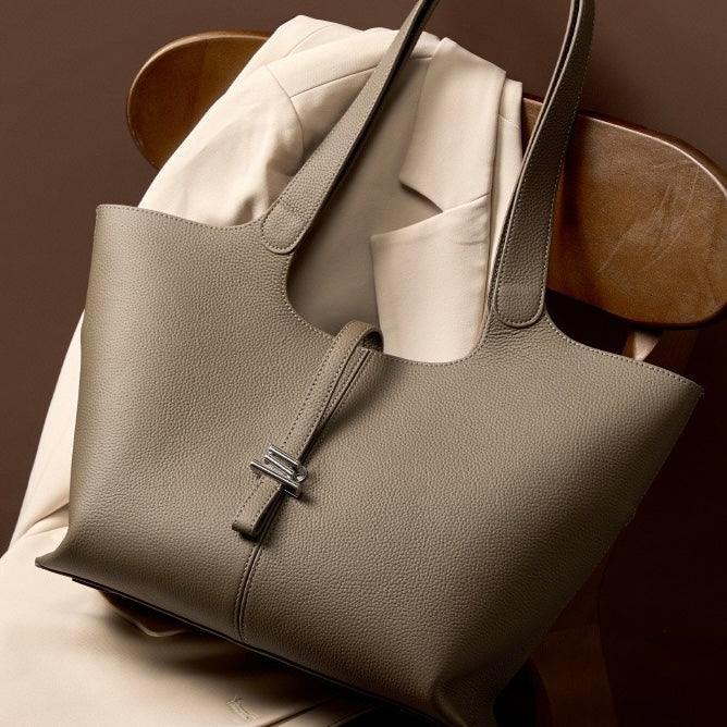 Taupe leather tote bag on beige blazer draped over wooden chair