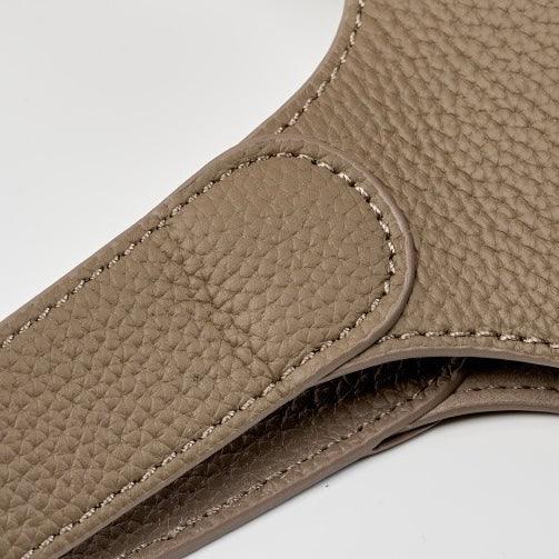 Closeup of taupe pebbled leather bag handle with detailed stitching on white background