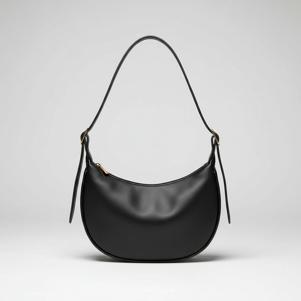 Black leather shoulder bag with curved shape on cream fabric, hand holding strap