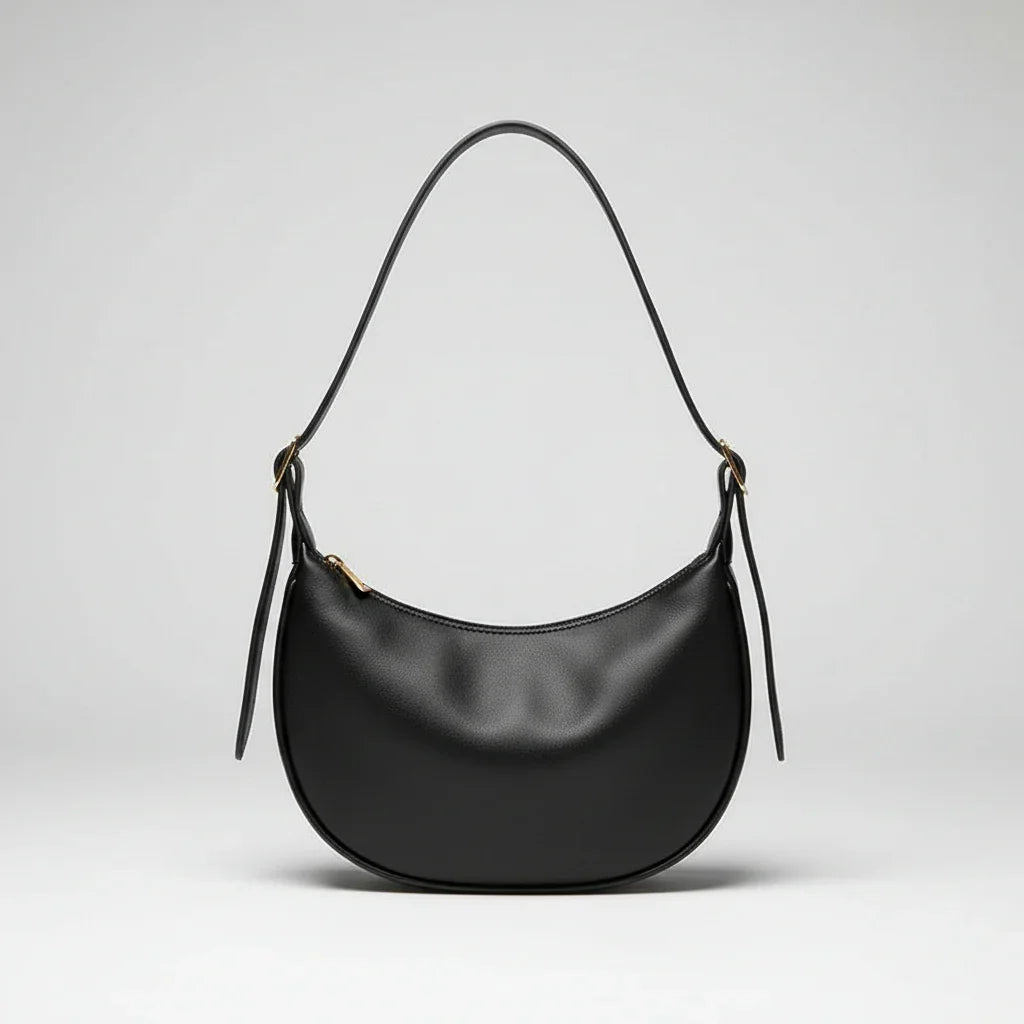 Black leather shoulder bag with curved shape on cream fabric, hand holding strap