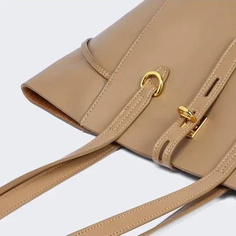 Beige leather handbag with gold hardware and adjustable shoulder strap on white background