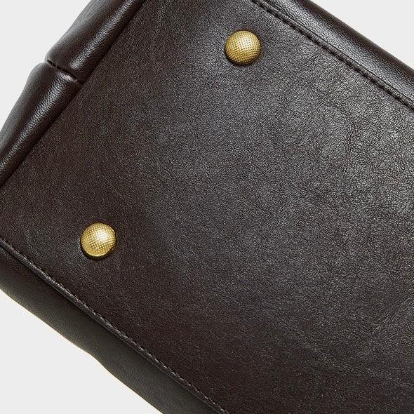 Close-up of brown leather bag bottom with gold metal feet on white background