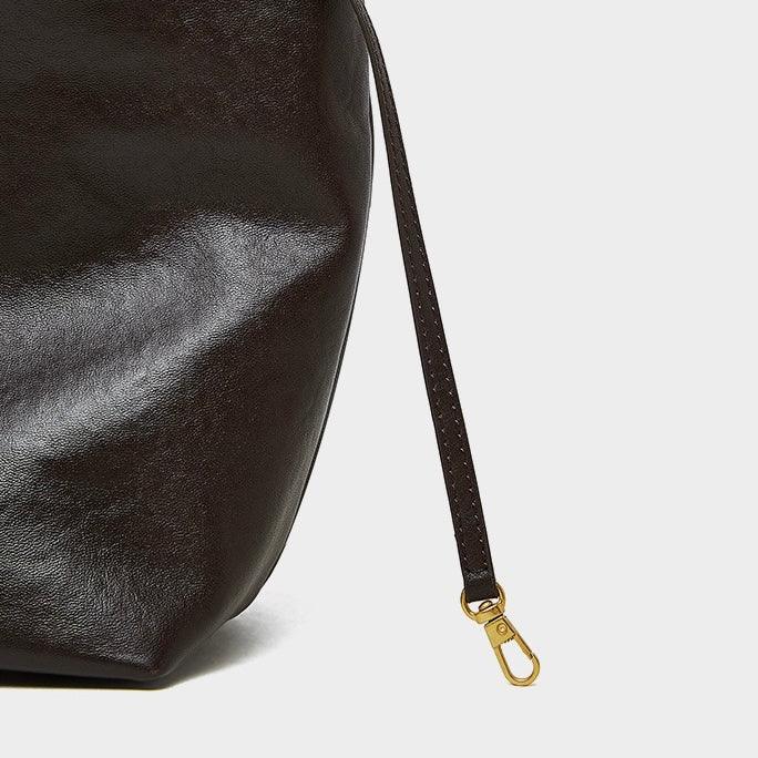 Close-up of dark brown leather bag with gold clasp on white background