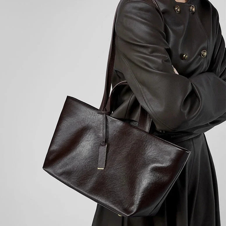 Woman in black trench coat carrying a sleek black leather tote bag