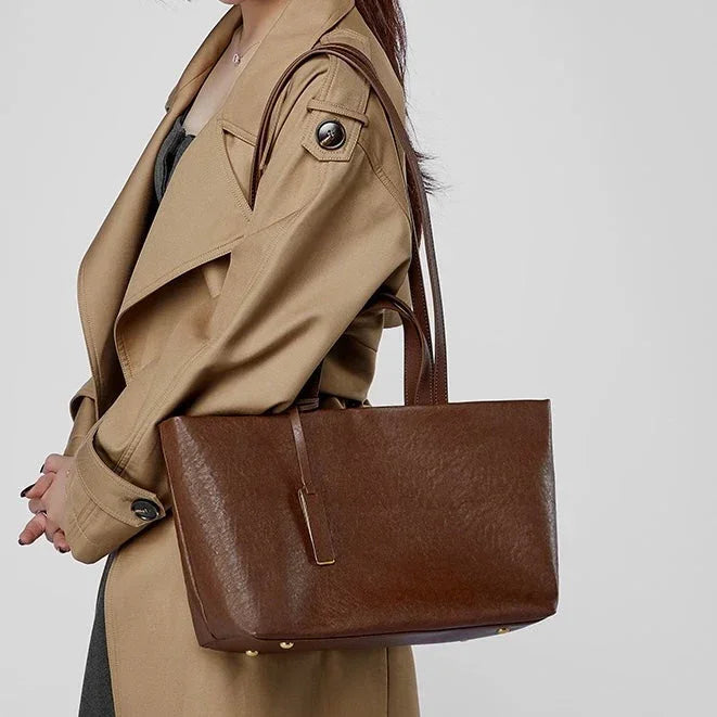 Woman in beige trench coat carrying large brown leather tote bag