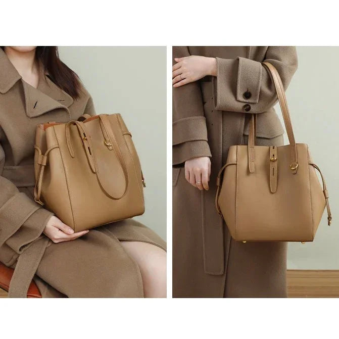 Tan leather tote bag with top handles, modeled with a beige wool coat indoors