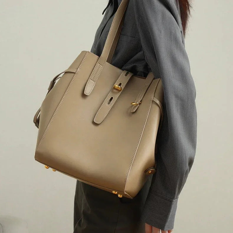 Woman wearing a taupe leather tote bag with gold hardware over a gray shirt