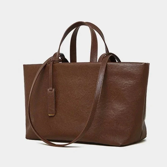 Brown leather tote bag with top handles and shoulder strap on a white background