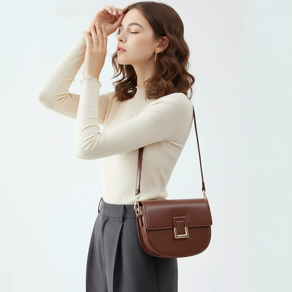 Woman wearing cream top and black pants with brown leather shoulder bag on white background