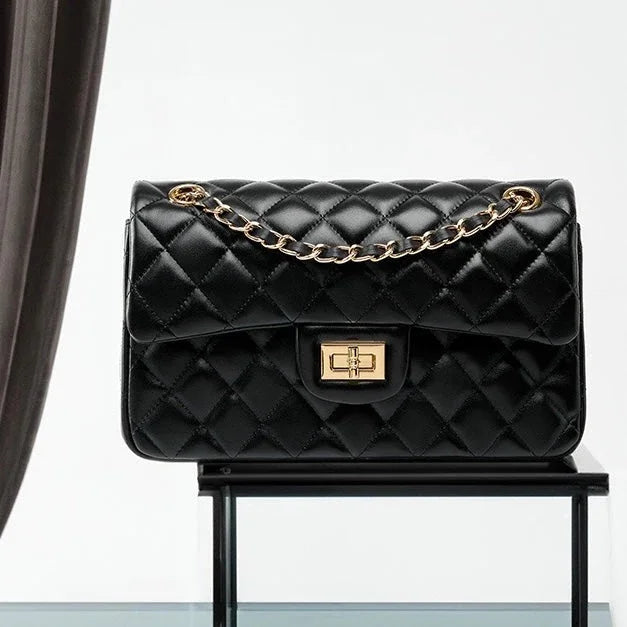 Black quilted leather handbag with gold chain strap and clasp on glass display