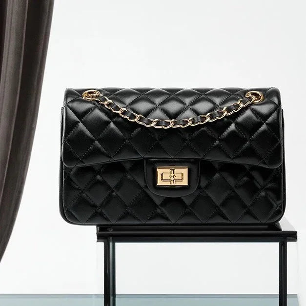 Black quilted leather handbag with gold chain strap and clasp on glass display