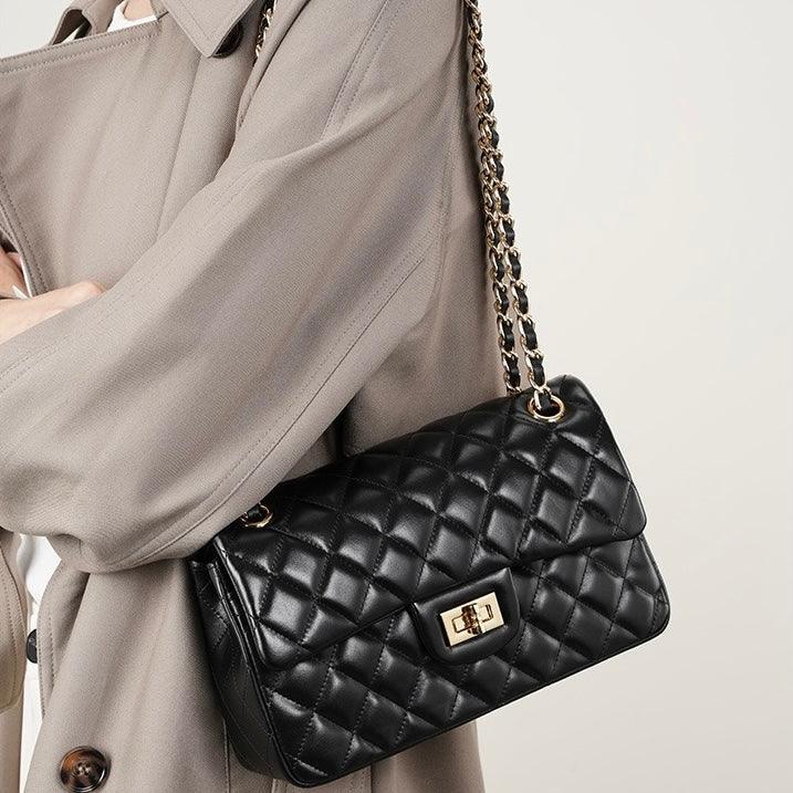 Woman wearing beige coat with black quilted leather shoulder bag and gold chain strap
