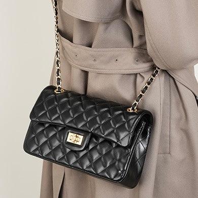 Black quilted leather shoulder bag with gold chain strap worn over a beige trench coat