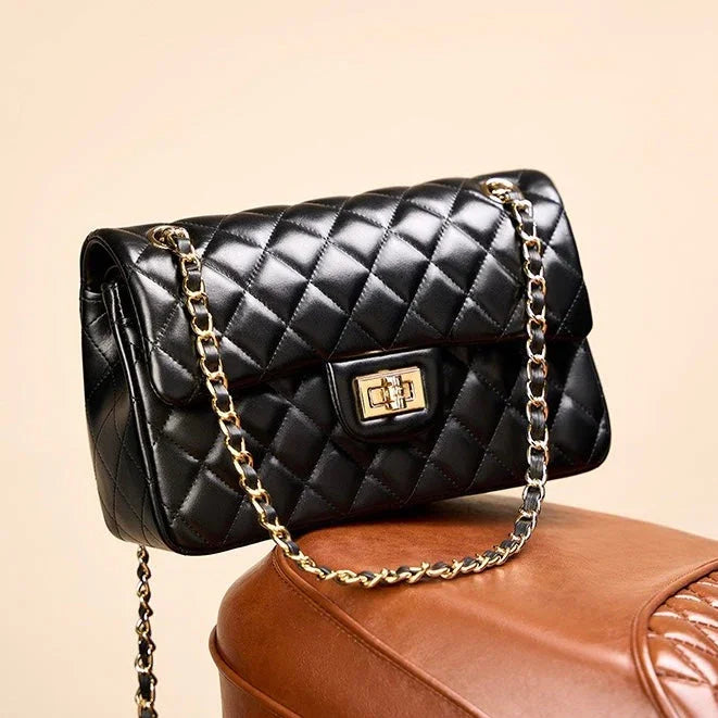 Black quilted leather shoulder bag with gold chain strap on brown leather surface