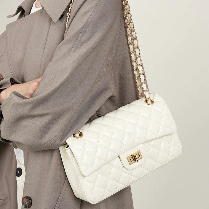 Woman in taupe trench coat carrying white quilted leather shoulder bag with gold chain strap
