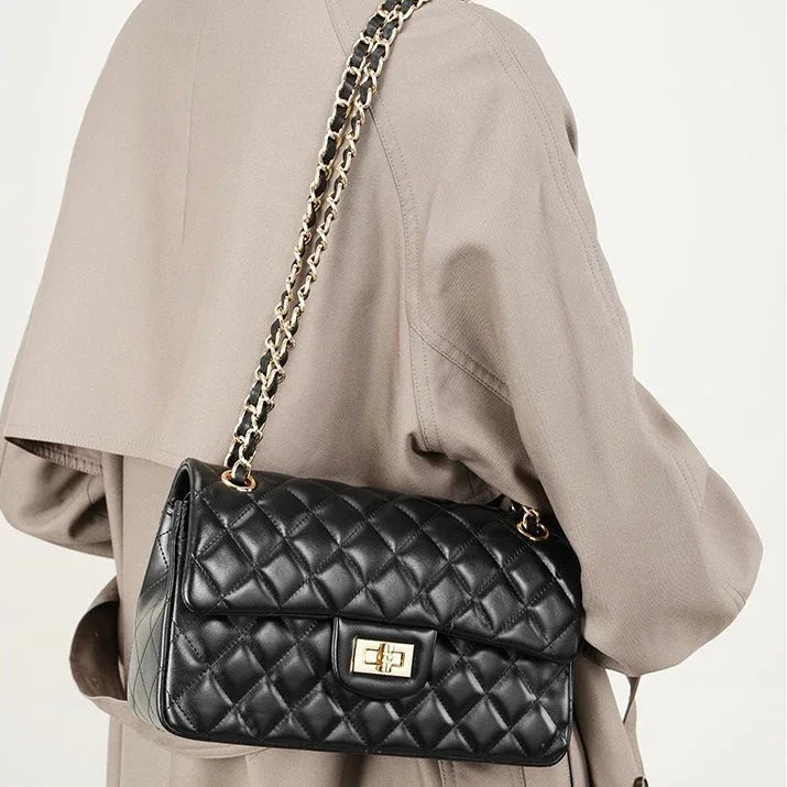 Quilted black leather shoulder bag with gold chain strap on beige coat