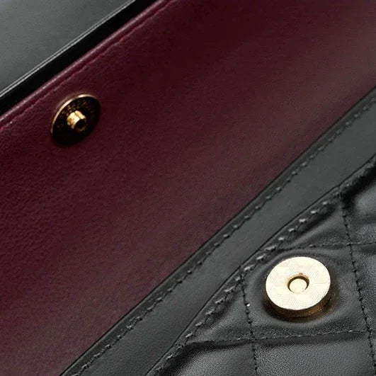 Closeup of quilted black leather bag with gold snap closure and burgundy interior