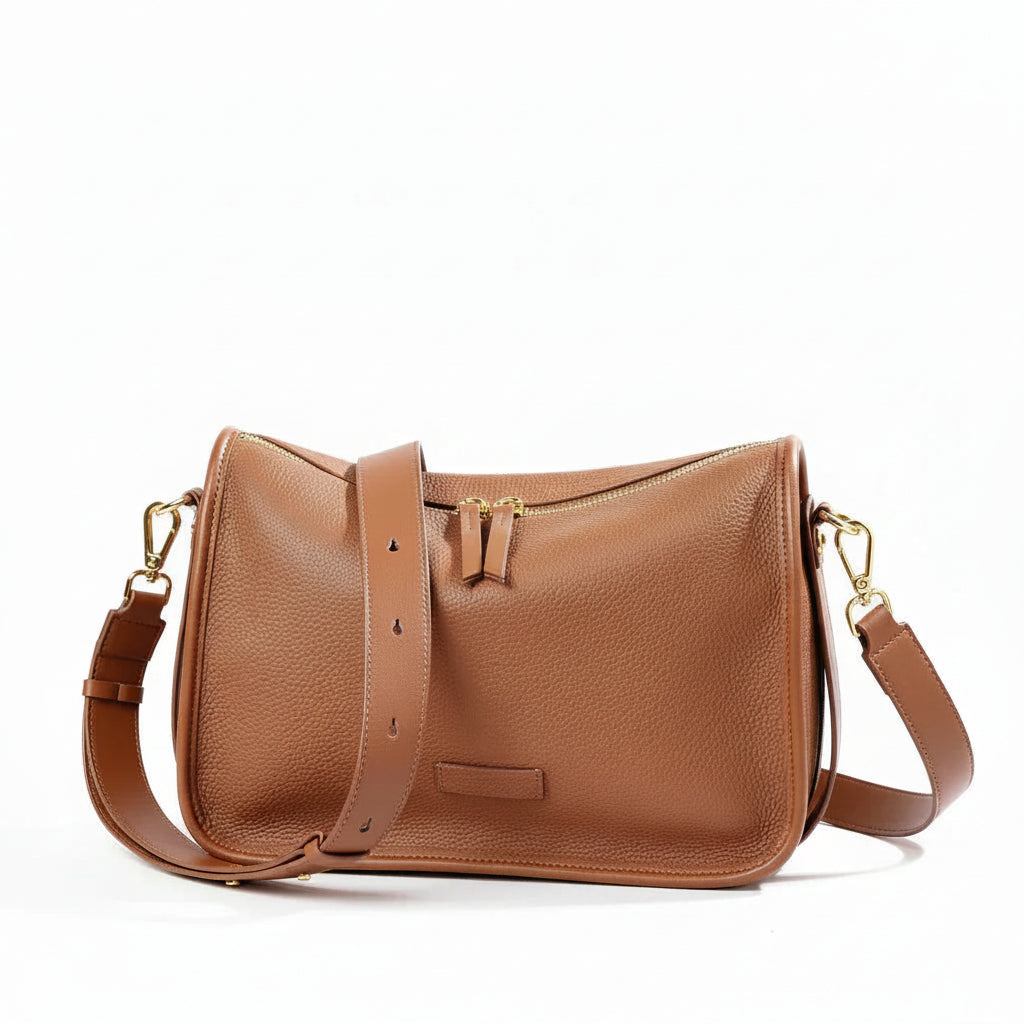 Tan leather crossbody bag with gold hardware and adjustable strap on white background