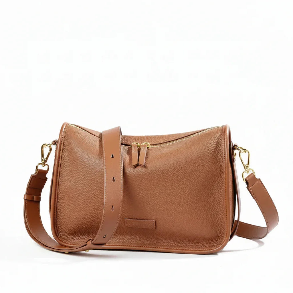Tan leather crossbody bag with gold hardware and adjustable strap on white background
