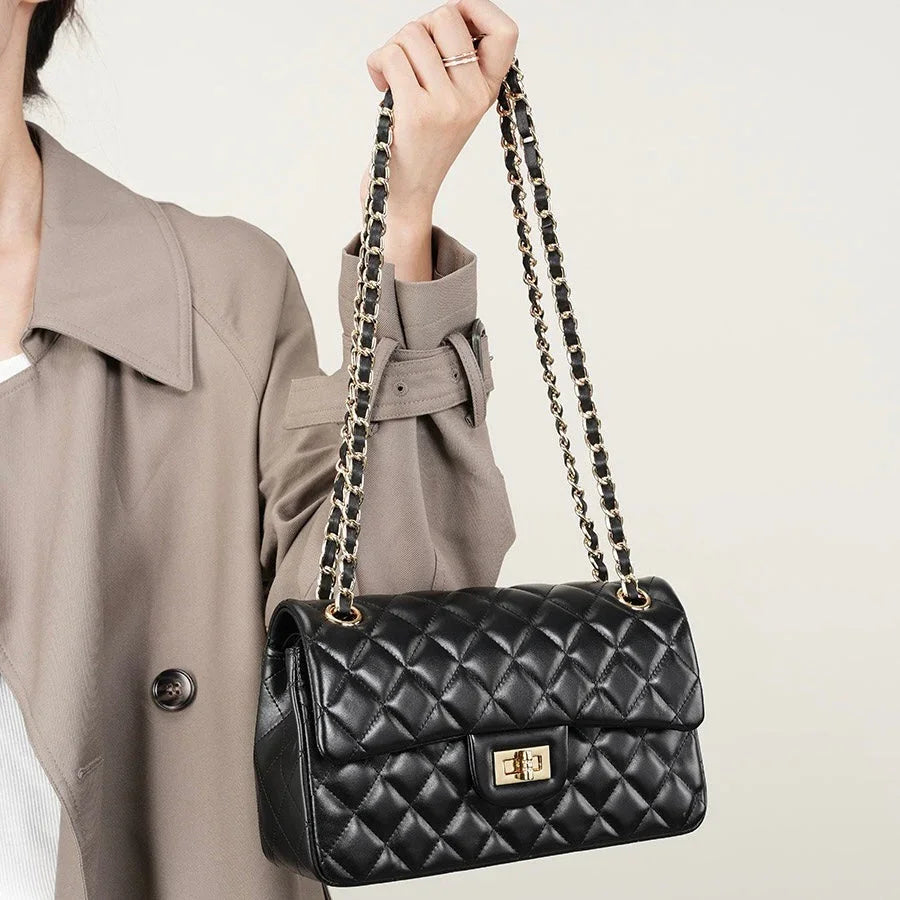 Woman holding black quilted leather shoulder bag with gold chain strap