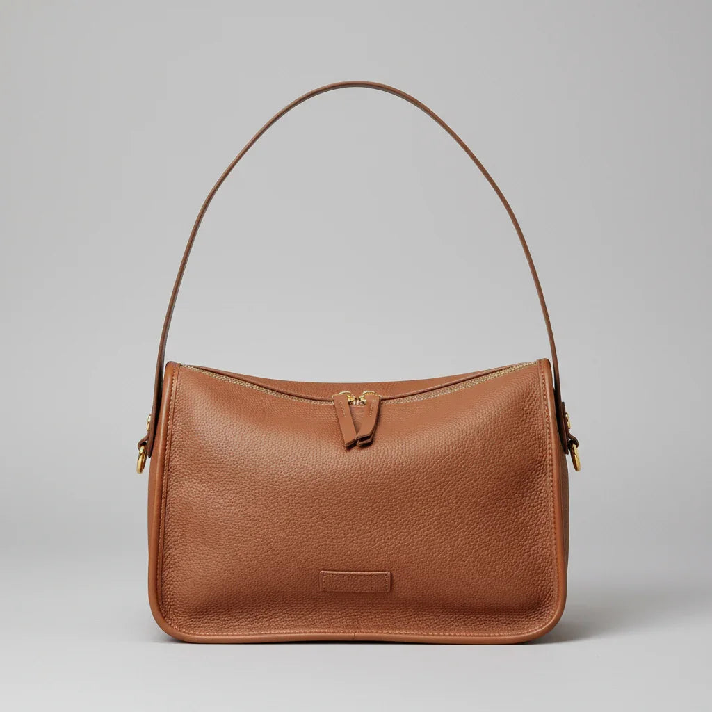 Brown leather shoulder bag with gold zipper on woven mat and wood background