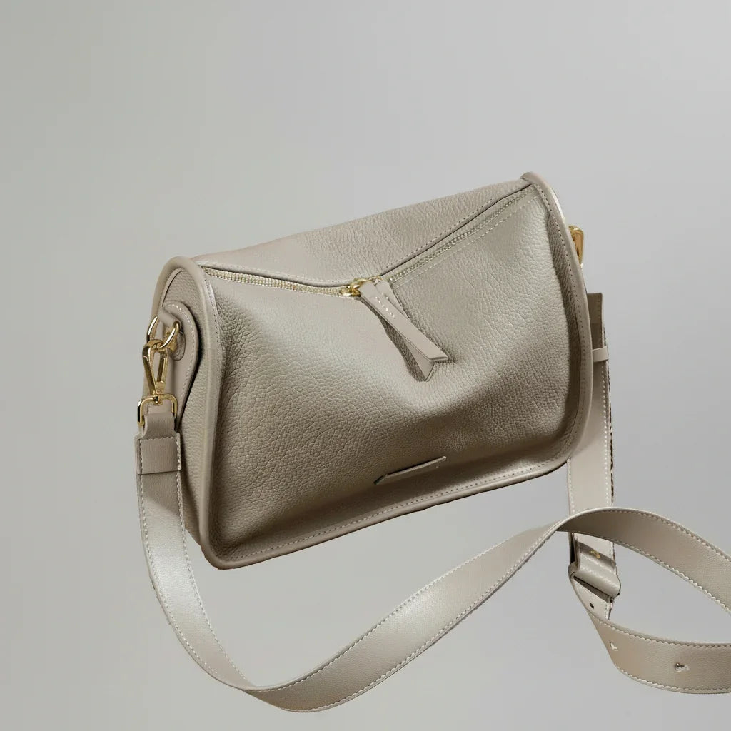 Taupe leather shoulder bag with gold hardware on woven surface, vintage clock in background