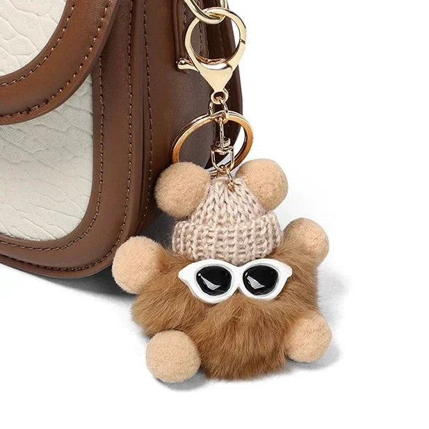Cute furry pom pom keychain with knit hat and sunglasses on brown leather bag