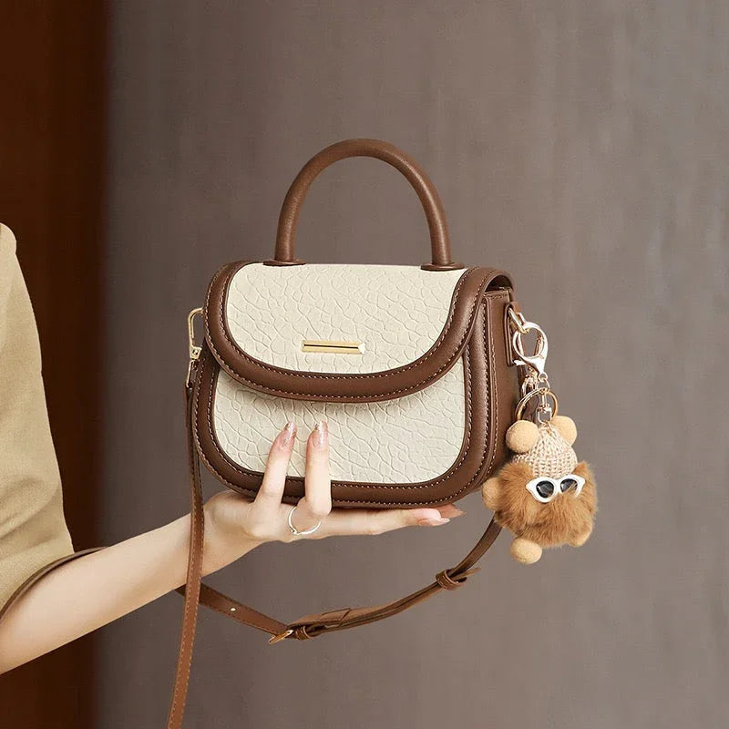 Stylish beige and brown leather handbag with top handle and cute plush keychain accessory