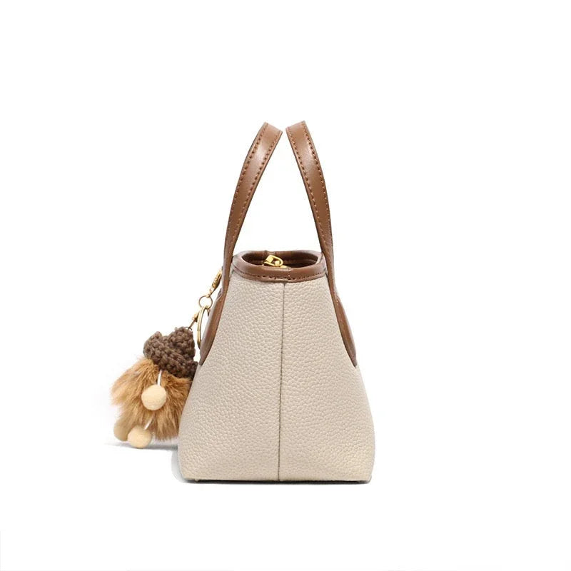 Side view of beige and brown leather handbag with plush keychain on white background