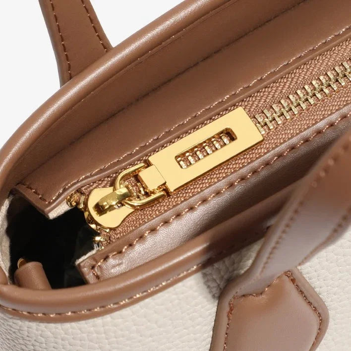 Close-up of brown leather handbag with gold zipper and textured beige exterior
