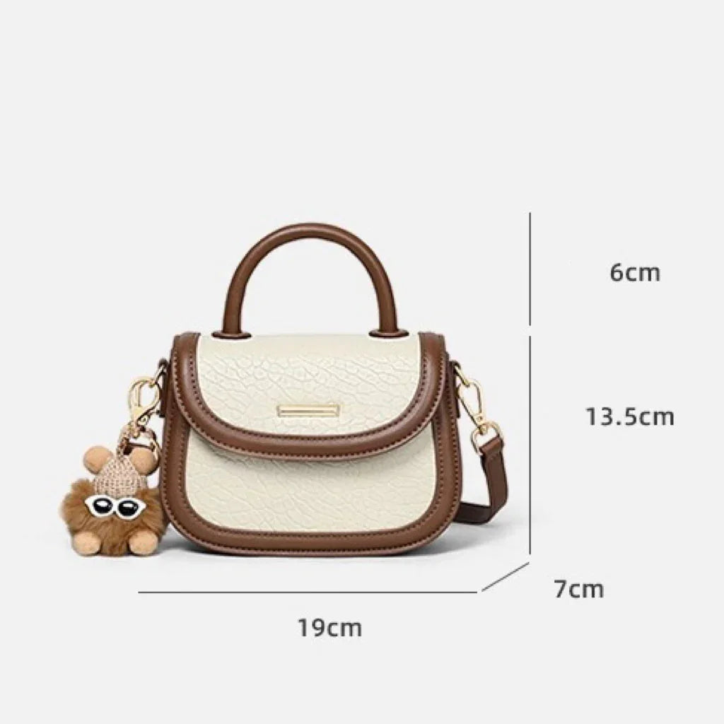 Small cream and brown leather handbag with top handle, toy keychain, and size measurements