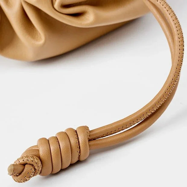 Tan leather drawstring bag with knotted strap detail on a white background