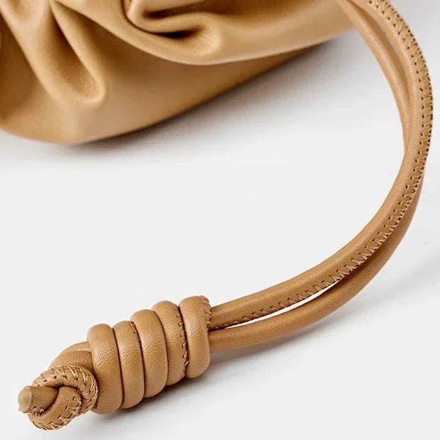 Tan leather drawstring bag with knotted strap detail on a white background