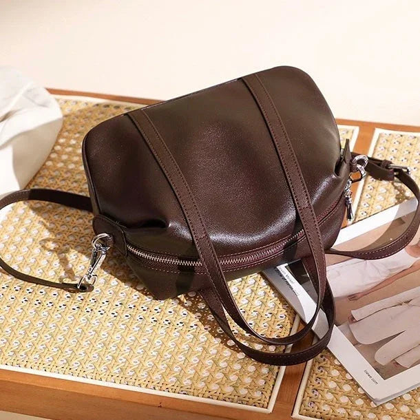 Dark brown leather crossbody bag on woven table with magazine and soft lighting