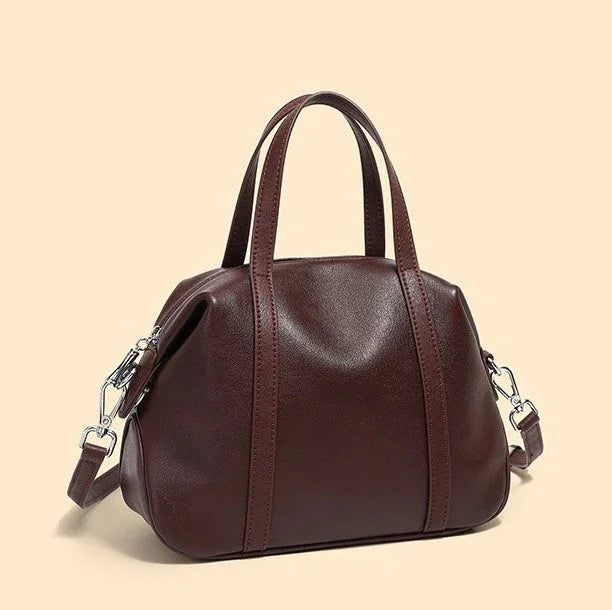 Brown leather handbag with top handles and detachable shoulder strap on beige background