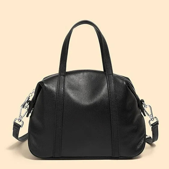 Black leather handbag with top handles and detachable shoulder strap on beige background