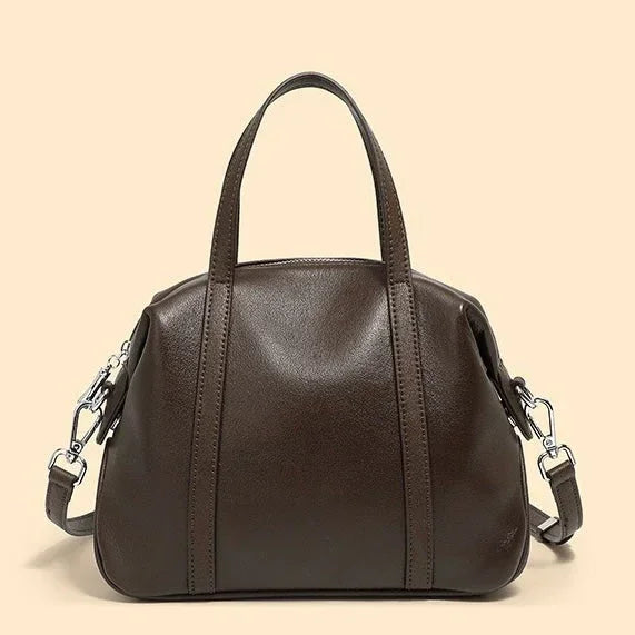 Brown leather handbag with handles and removable shoulder strap on beige background