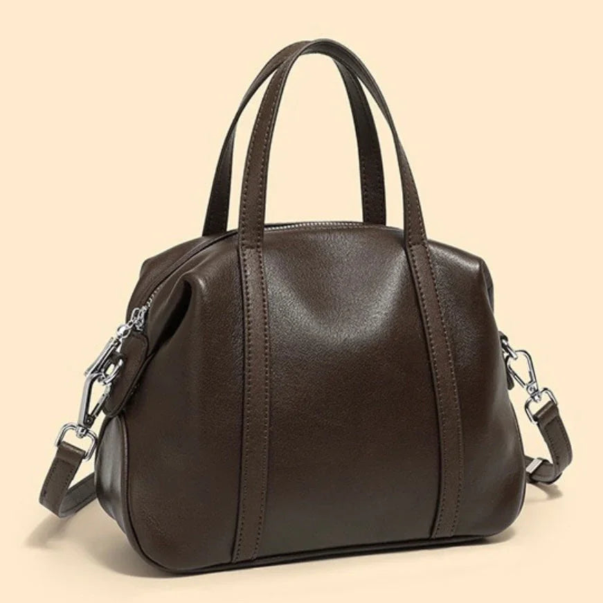 Dark brown leather handbag with top handles and shoulder strap on beige background