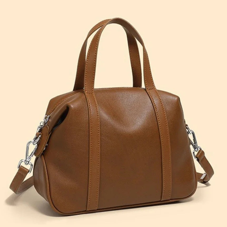 Brown leather handbag with top handles and shoulder strap on beige background