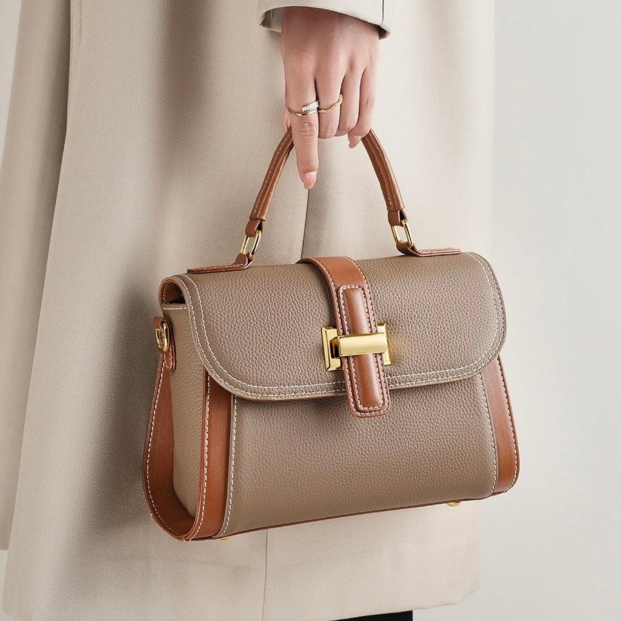 Woman holding taupe and brown leather handbag with gold hardware, wearing beige coat