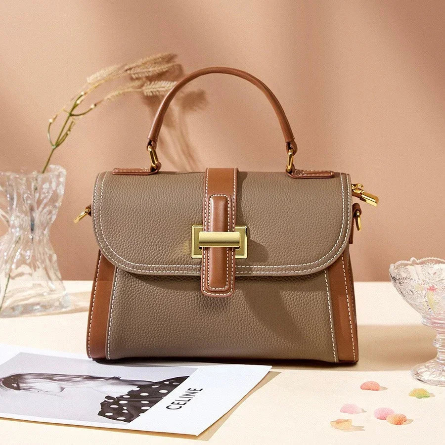 Taupe and brown leather handbag with gold buckle on beige table, elegant fashion accessory