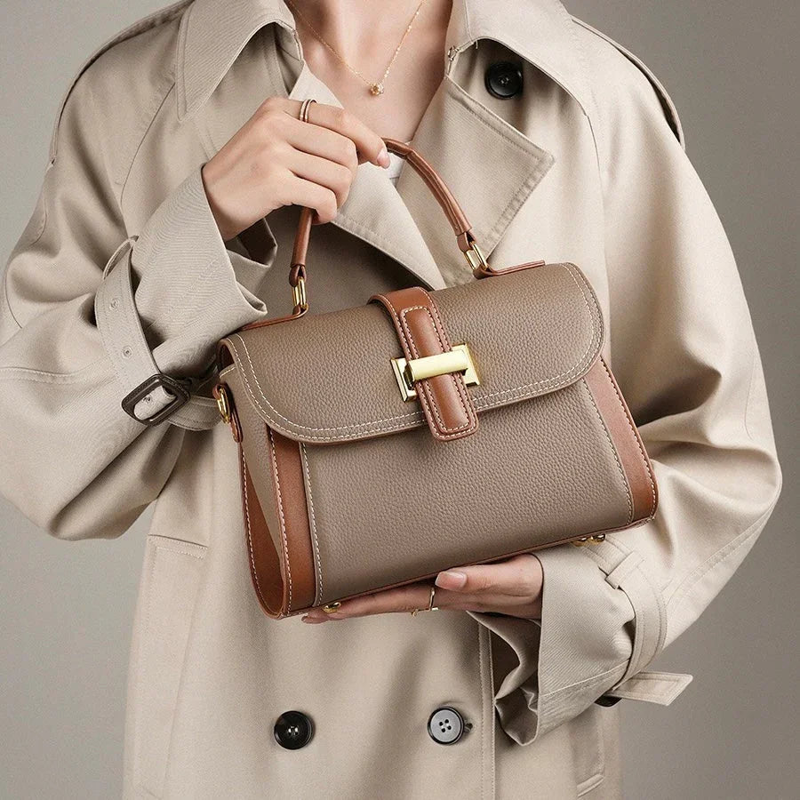 Woman in beige trench coat holding taupe leather handbag with gold buckle