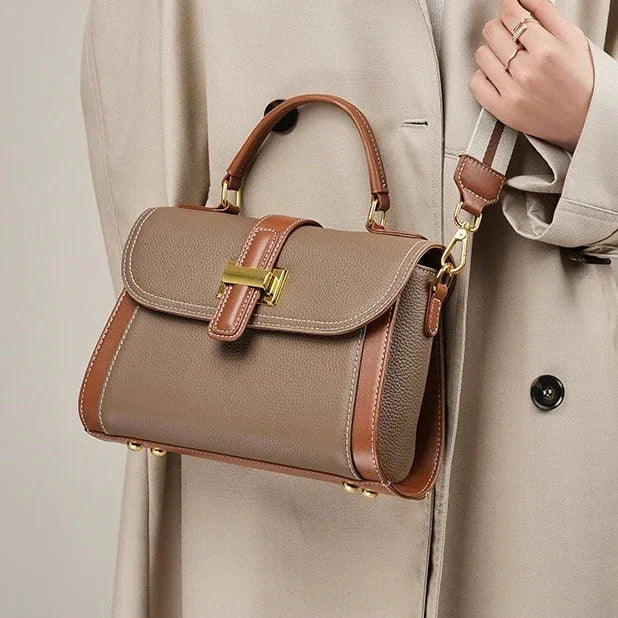 Classic taupe leather handbag with brown trim and gold hardware, worn over beige coat