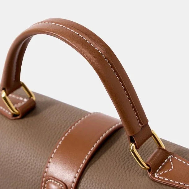 Close-up of brown leather handbag handle with gold hardware and white stitching