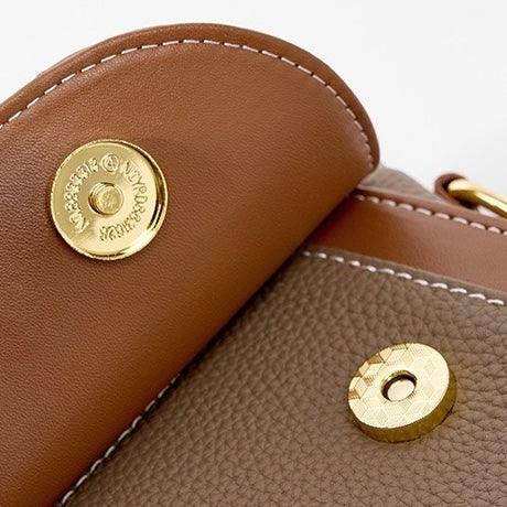 Close-up of brown leather bag with gold magnetic snap clasp and white stitching